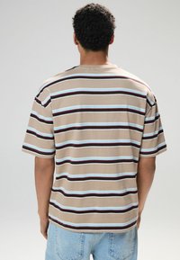 Stribet t-shirt i beige med blå, brun og hvide vandrette striber. Korte ærmer og en afslappet pasform. Blød tekstur, rund halsdesign.