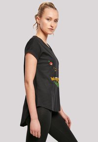 Black cotton t-shirt with short sleeves, featuring colorful graphic text and cartoon design. Curved hemline, worn with black leggings.