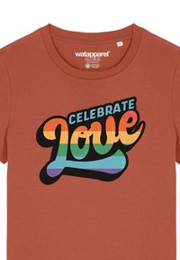 Baumwoll-T-Shirt mit kurzen Ärmeln in Rostfarbe, das mit einer auffälligen "Celebrate Love"-Grafik in Regenbogenfarben und einem schwarzen Umriss versehen ist.