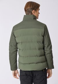 Giubbotto imbottito di colore verde oliva, con colletto alto e design trapuntato. Il materiale appare liscio con una texture leggermente lucida.