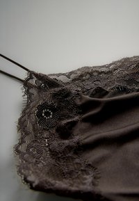 Melns satīna krekliņš ar mežģīņu apdari gar kakla izgriezumu, plānām regulējamām siksniņām un gludu tekstūru.