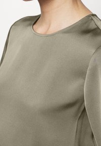 Olivgrünes Satinoberteil mit runder Halslinie und glatter Textur, kurzen Ärmeln und minimalistischem Design.