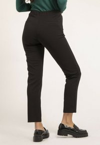 Pantalons noirs, ajustés, avec une coupe slim et une longueur cheville. Fabriqués en tissu lisse avec deux poches arrière et une taille haute. Associés à des mocassins noirs.
