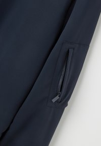La manga de la chaqueta azul marino presenta un tejido suave, un bolsillo con cremallera con una elegante pestaña y costuras ajustadas a lo largo de la costura.