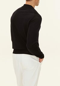 Svart stickad tröja med en åtsittande design och ribbad nederkant, med en klassisk krage och långa ärmar. Bärs tillsammans med vita byxor.