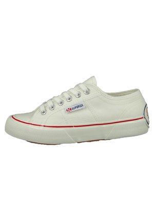 White canvas sneakers with a textured upper, rubber sole, red stripe, and metallic eyelets, featuring a small logo patch on the side.