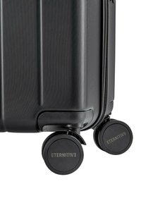 Czarna walizka z twardą skorupą, z teksturowaną powierzchnią, wyposażona w podwójne obrotowe kółka i zamknięcie na zamek błyskawiczny. Na kółkach widoczna jest marka "ETERNITIV3".