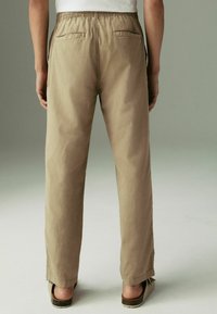 Beige, gumis derékú nadrág, két hátsó zsebbel, egyenes lábszár dizájnnal, pamut anyagból készült, enyhe textúrával. A lábbeli ívelt sarkú.