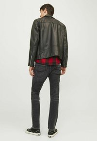 Chaqueta de biker de cuero negro con un diseño ligeramente recortado, combinada con jeans de mezclilla oscura y zapatillas negras. Camisa de franela roja y negra debajo.