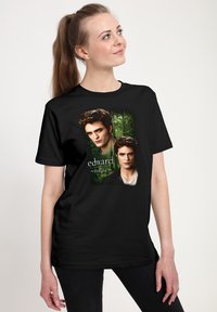 Žena s dlouhým copem, která má na sobě černé tričko s portréty Edwarda ze ságy Stmívání na pozadí lesa.