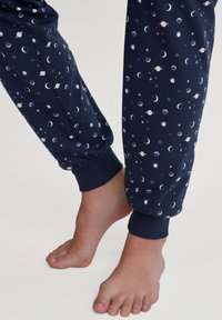 Marine blauwe katoenen pyjamabroek met een ruimteschema met planeten, manen en sterren. Ribbelboorden bij de enkel. Gladde textuur.