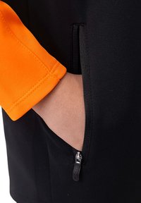 Schwarze Jacke mit einem orangefarbenen Ärmel; verfügt über eine Reißverschlusstasche an der Seite. Das Material wirkt glatt und hat einen leichten Glanz.