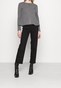 Veste grise zippée avec un design à basque, tissu texturé, manches longues, associée à un pantalon noir à jambes droites et des bottines noires.