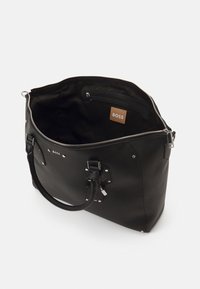 Black leather tote bag with textured surface, zip closure, interior pocket, silver hardware accents, and a visible brand label inside.