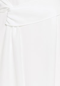 Bílé saténové šaty s propleteným uzlem v pase. Hladká textura, splývavá tkanina a volný design vytvářejí elegantní siluetu.