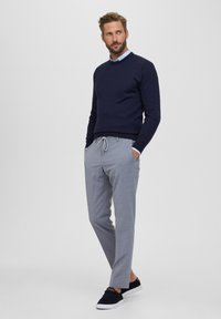 Maglione a maglia blu, pantaloni grigi su misura con coulisse e sneaker blu. Linee pulite e un look casual con tessuti a contrasto e texture.