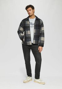 Plaid jacket in navy, cream, and gray wool blend; zip closure; worn over a light blue t-shirt and dark jeans; paired with light sneakers.