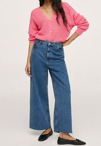 Vaaleanpunainen, paksu neulecardigan, jossa on V-pääntie ja napit, yhdistetty korkeavyötäröisiin, leveälahkeisiin sinisiin farkkuihin ja mustiin ballerinatossuihin.