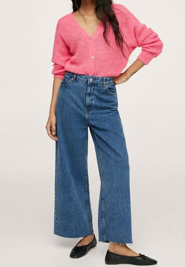 Vaaleanpunainen, paksu neulecardigan, jossa on V-pääntie ja napit, yhdistetty korkeavyötäröisiin, leveälahkeisiin sinisiin farkkuihin ja mustiin ballerinatossuihin.