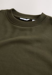 Mörkgrön sweatshirt med ribbad rund halsringning och mjukt, texturerat tyg. Har en ren design utan synliga mönster eller detaljer.