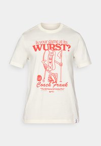 Short-sleeve cream t-shirt with red graphic text and cartoon hot dog character holding a golf club and flag, featuring rounded neckline and hem tag.