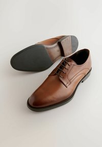 Brązowe skórzane buty do garnituru o gładkim wykończeniu, zaokrąglonym nosku, sznurowanym kroju oraz gumowej podeszwie z teksturowanym gripem i detalami haftu.