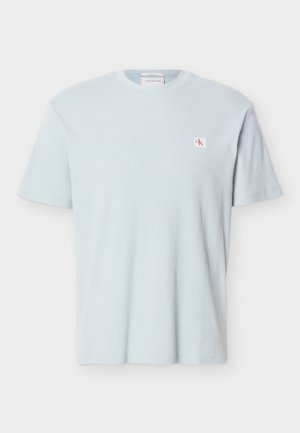 Camiseta de manga corta de punto waffle azul claro con cuello redondo y pequeño parche con el logo "CK" en rojo y blanco en el lado izquierdo del pecho.