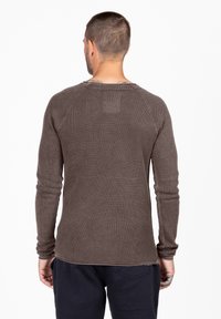 Camicia a maniche lunghe in tessuto marrone scuro e strutturato; presenta un collo arrotondato e maniche raglan, design minimalista senza motivi visibili.