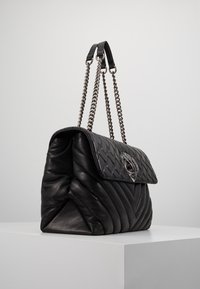 Quiltowana torebka skórzana w kolorze czarnym z klapą, srebrny łańcuszek oraz dekoracyjne okucia z przodu. Gładka faktura i zdefiniowany kształt.