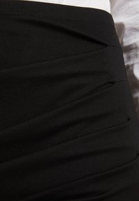 Černá elastická sukně má řasený design, měkkou látku, hladkou texturu a přiléhavý střih s elastickým pasem.