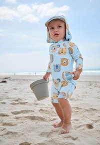 Light blue, short-sleeved rash guard featuring cartoon animal patterns. The child holds a gray bucket, standing on sandy beach.