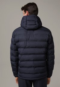 Navy blue puffer jacket with a hood, quilted design, elastic cuffs, and a smooth texture. Includes a small, rectangular label on the back.
