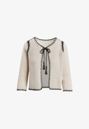 Krēmkrāsas adīta jakas ar melniem akcentiem, atvērta priekšpuse, trīs ceturtdaļu garuma piedurknes un saišu aizdare ar pērlītēm. Visā virsmā ir teksturēts raksts.