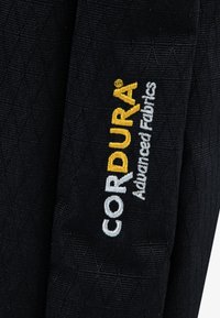 Μαύρο υφασμάτινο υλικό με υφή, που φέρει το κέντημα "CORDURA® Advanced Fabrics" σε λευκό και κίτρινο χρώμα. Το υλικό έχει διακοσμητικό μοτίβο με διαμάντια.