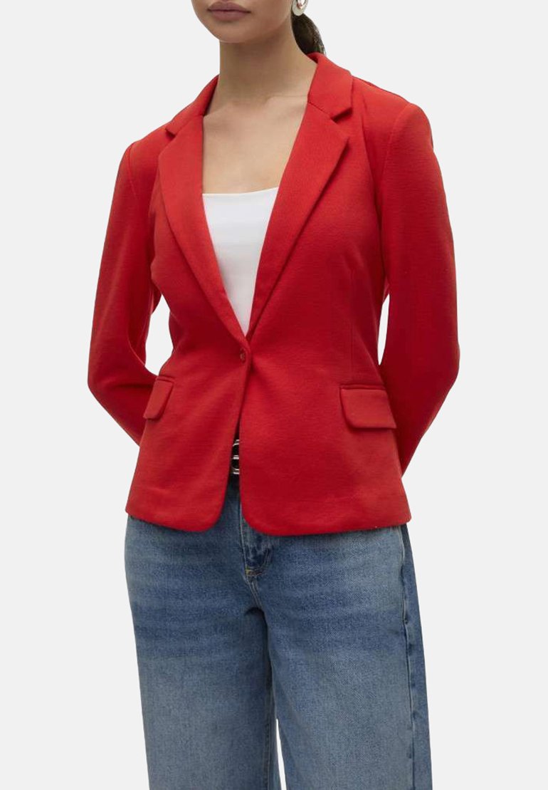 Blazer structuré rouge avec revers, fermeture à un bouton unique et poches avant. Porté par-dessus un haut blanc et un jean large bleu.