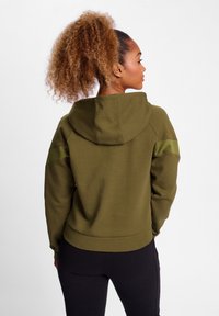 Olive green hoodie with a hood and contrasting shoulder panels. Features a relaxed fit and soft texture. Worn with black leggings.