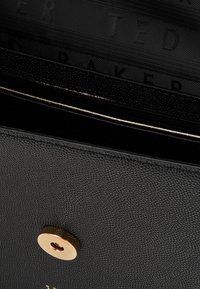 Portafoglio nero in materiale sintetico, con chiusura a scatto dorata e marchio discreto all'interno.