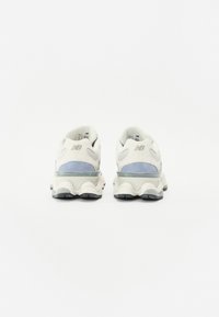 White and blue sneakers featuring a mesh and suede upper, wavy sole design, and a transparent midsole, with a prominent logo at the heel.