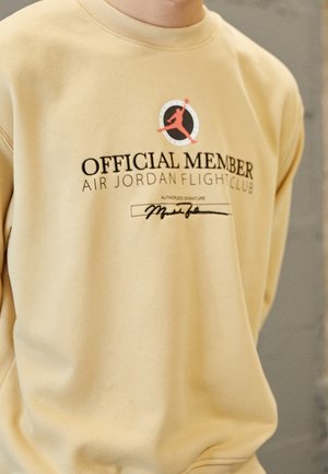 Beige sweatshirt med Air Jordan Flight Club-logo, teksten "Official Member" og en sort signatur under teksten på en persons overkrop.