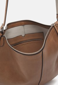 Sac à main en cuir marron avec une finition texturée, fermeture éclair, et un compartiment intérieur gris clair avec une poche zippée et un emplacement pour cartes.