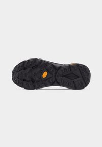 Το πάτημα της σόλας ενός μαύρου παπουτσιού Vibram με τραχιά, πολυκατευθυντικά πέλματα και πορτοκαλί λογότυπο Vibram κοντά στο κέντρο.