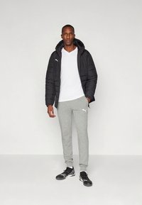 Svart vattert jakke, hvit t-skjorte, grå joggebukser med logo og svarte joggesko. Elegant design, minimal fargekontrast, urbant stil.