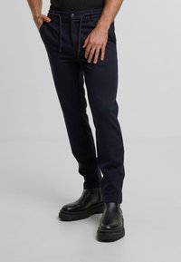 Navy broek van zachte stof met een taps toelopend ontwerp, voorzien van een elastische koordtailleband en zijzakken, gecombineerd met zwarte chunky laarzen.