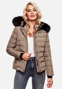 Beige pufferjakke med hætte i sort pelskant, quiltet design, lynlås foran og sorte ribbede manchetter, båret over en hvid top og jeans.