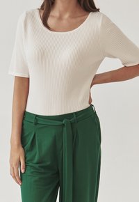 Vit ribbad kortärmad topp i kombination med gröna hög midja byxor som har en frontknut, strukturerad passform och subtila texturdetailler.