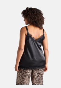 Camisola nera in satin con bordo in pizzo lungo il scollo e l'orlo, dotata di spalline regolabili. Abbinata a pantaloni corti con stampa leopardata.
