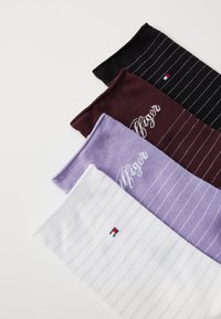 Quatre paires de chaussettes avec des rayures noires, bourgogne, lavande et blanches. Le matériau est un tricot doux ; les chaussettes présentent des logos de marque dans des couleurs contrastées.