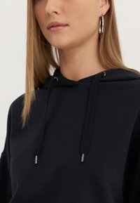 Black hooded sweatshirt made of cotton, featuring drawstrings with metal tips, ribbed detailing, and a relaxed fit.