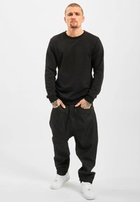 Black sweatshirt with long sleeves, paired with loose, dark gray pants. White sneakers complete the outfit. No visible patterns or accents.