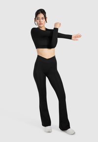 Zwarte langemouwen crop top met een aansluitend ontwerp en hoge zwarte flare-panten. De stof lijkt glad en rekbaar.
